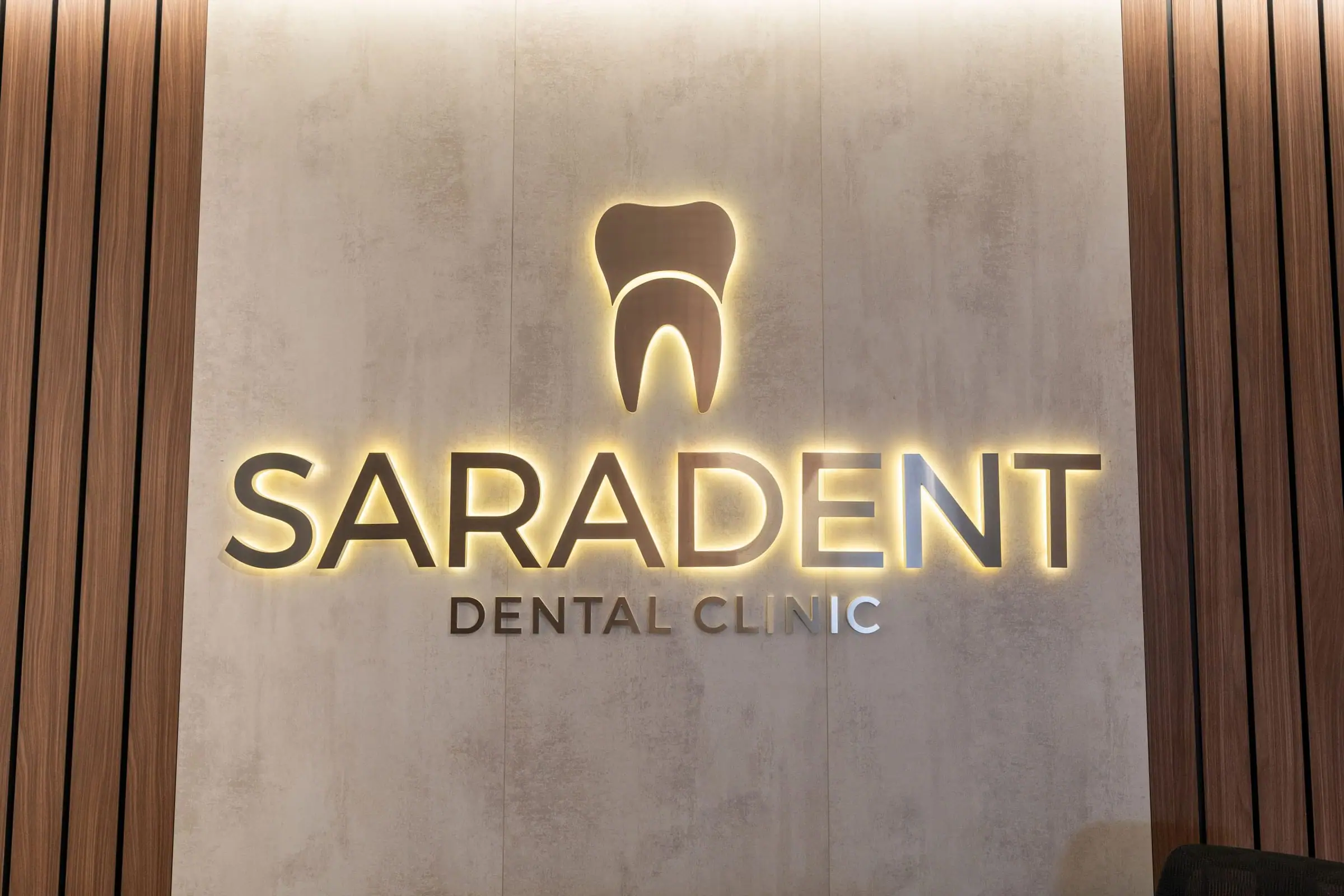Verlichte gouden letters Saradent Dental Clinic aan de wand van de receptie